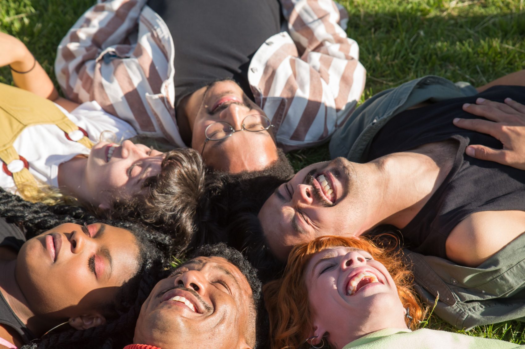 A group of friends lying together in the grass, laughing in warm sunshine